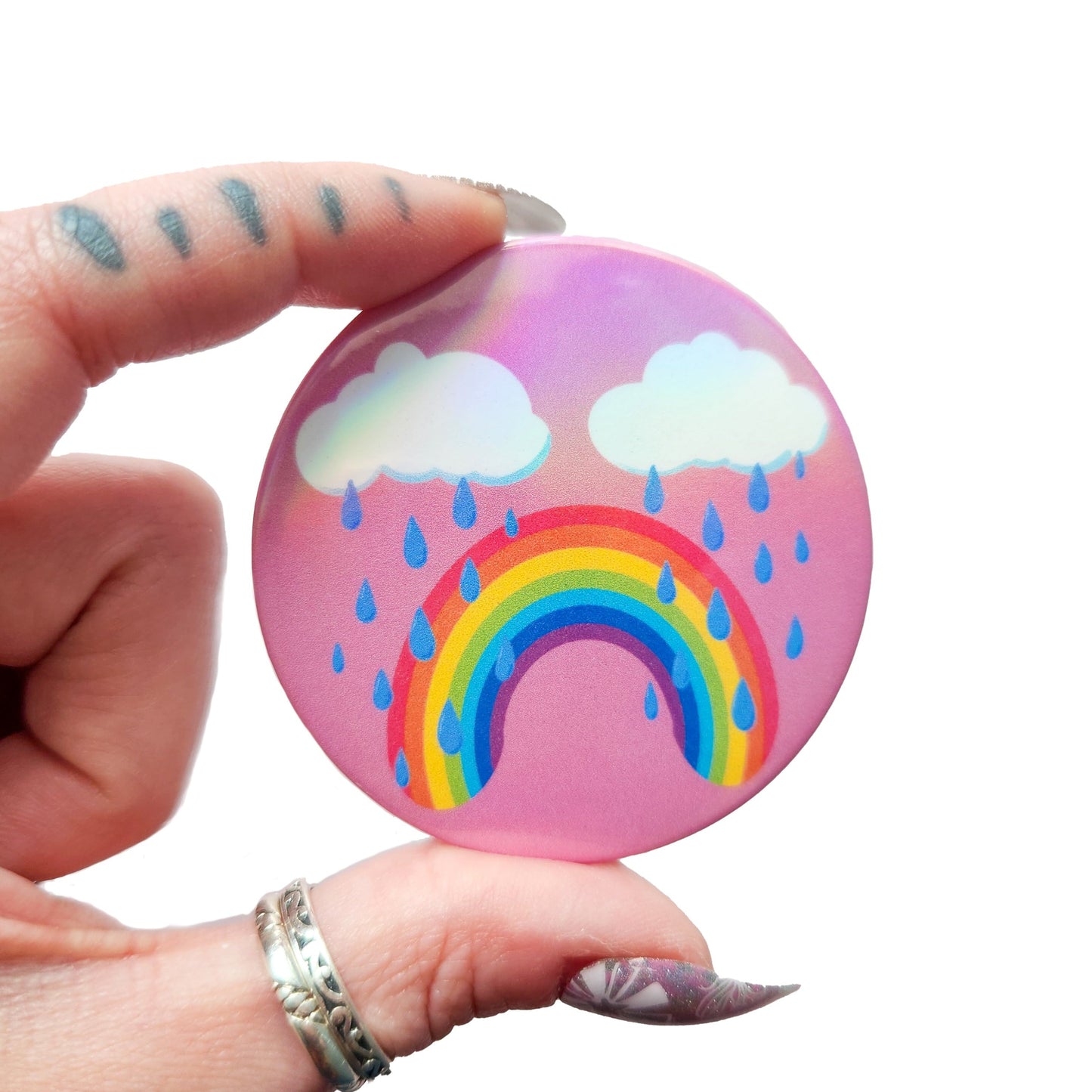 Bittersweet rainbow holographic button pin with a pink background, featuring a crying rainbow under two clouds with raindrops