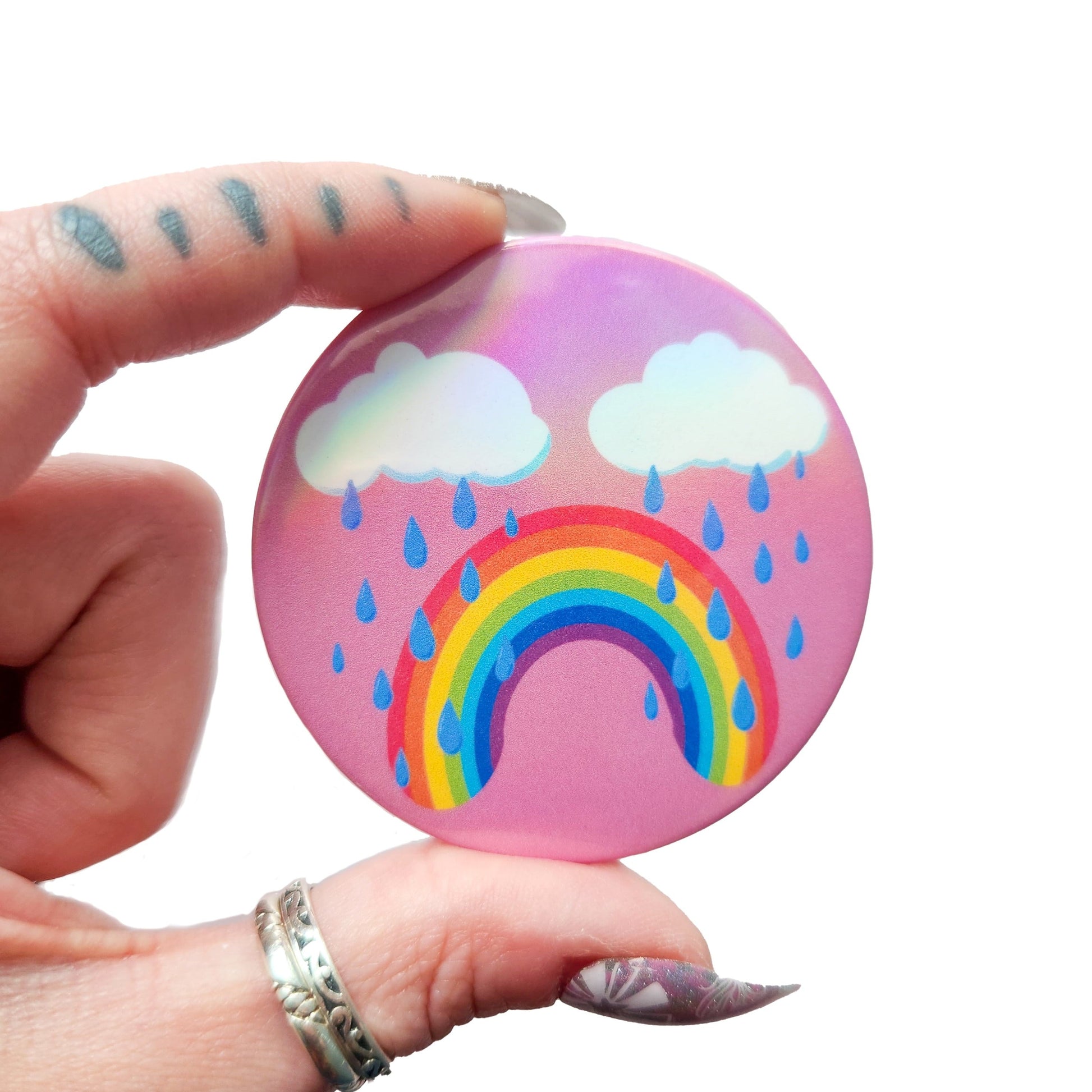 Bittersweet rainbow holographic button pin with a pink background, featuring a crying rainbow under two clouds with raindrops